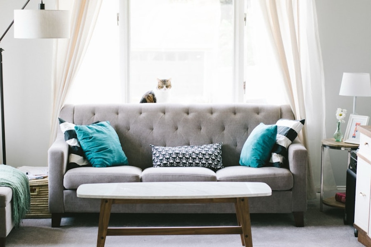 A living room with a grey tufted sofa and teal cushions, photographed before redesign